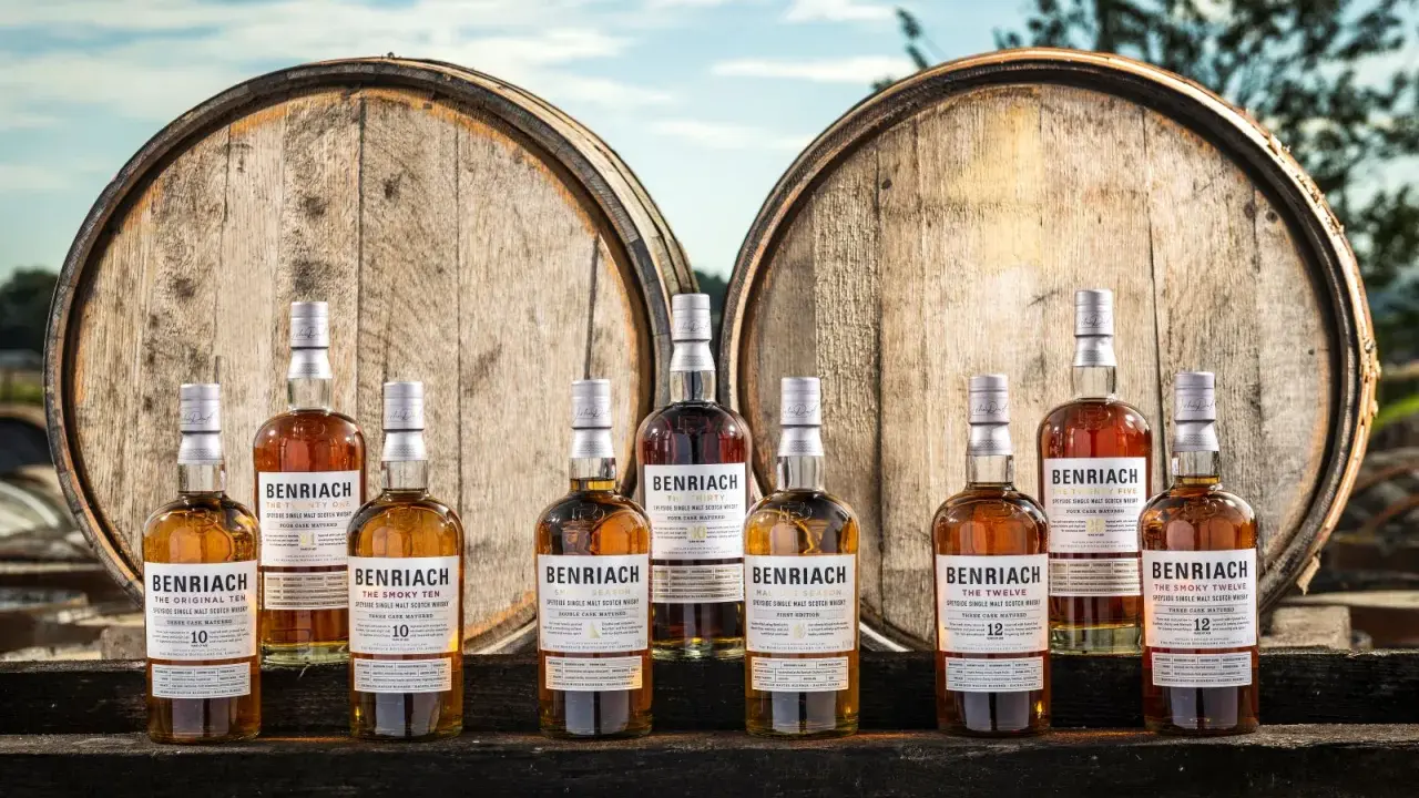 Butelki whisky BenRiach stoją przed beczkami, które zdradzają, skąd pochodzi whisky.