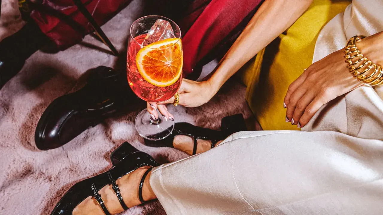 Elegancka kobieta z drinkiem, w którym widać plaster pomarańczy i lód. Zastanawiasz się, wermut co to? To aromatyzowane wino, idealne na letnie wieczory.