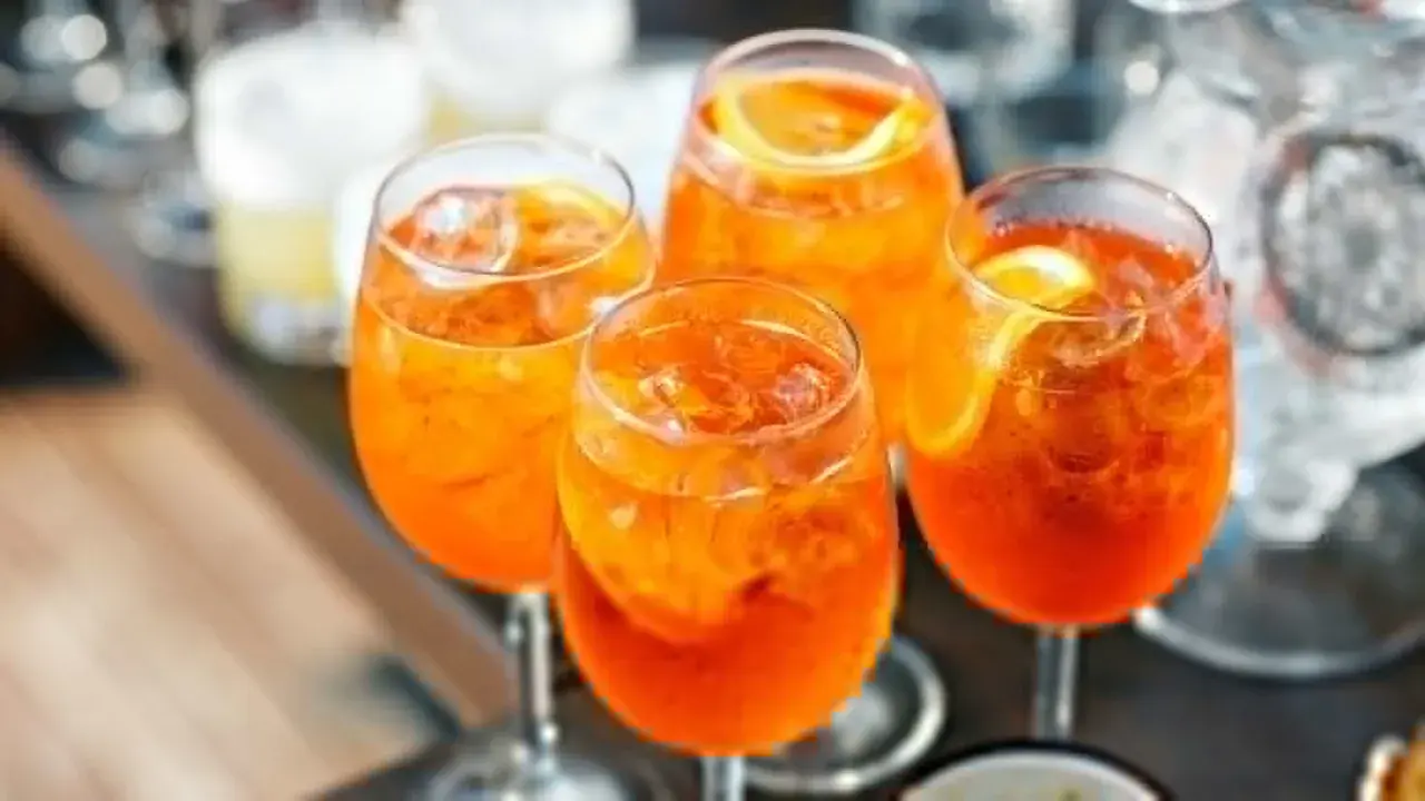 Cztery orzeźwiające Aperol Spritz z lodem i plasterkami pomarańczy, gotowe do świętowania lata.