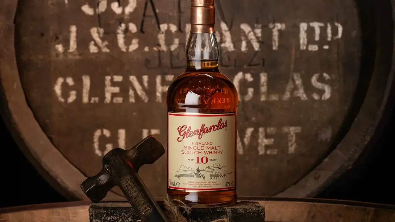 Butelka Glenfarclas 10 Year Old, jedna z 10 najlepszych whisky, na tle beczki. Młotek sugeruje rzemiosło.