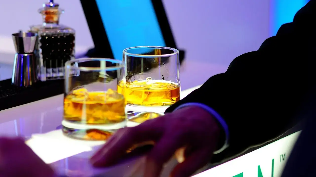 Dwa kieliszki złocistej whisky na barze, idealne na dzień whisky. Dłoń w garniturze sięga po drinka.