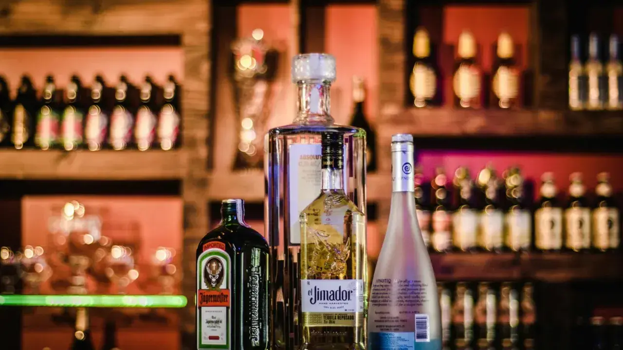 Butelki alkoholi na półce barowej: Jägermeister, tequila El Jimador, Absolut i Hypnotiq. Czy wiesz, whisky ile procent ma?