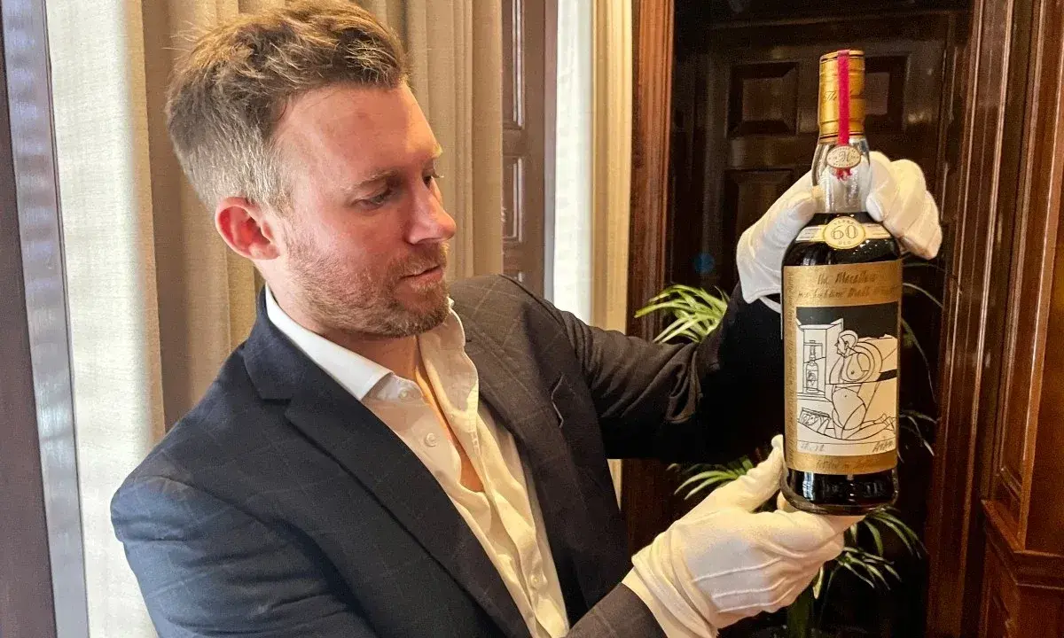 Mężczyzna w białych rękawiczkach prezentuje butelkę The Macallan 60 Year Old, jedną z najdroższych whisky świata.