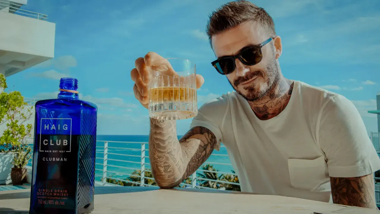 David Beckham z kieliszkiem Haig Club whisky, na tle błękitnego nieba i morza. Idealny moment na relaks.