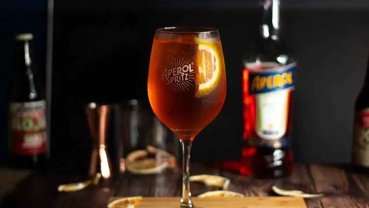 Orzeźwiający Aperol Spritz z plastrem pomarańczy, obok butelki Aperolu. Poznaj różne rodzaje Aperolu i jego zastosowania.