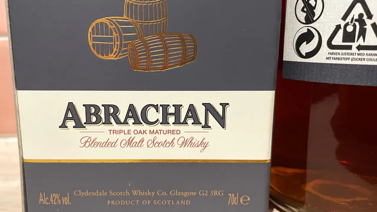 Elegancka butelka Abrachan Blended Malt Scotch Whisky, potrójnie dojrzewająca w dębie, z beczkami na etykiecie.