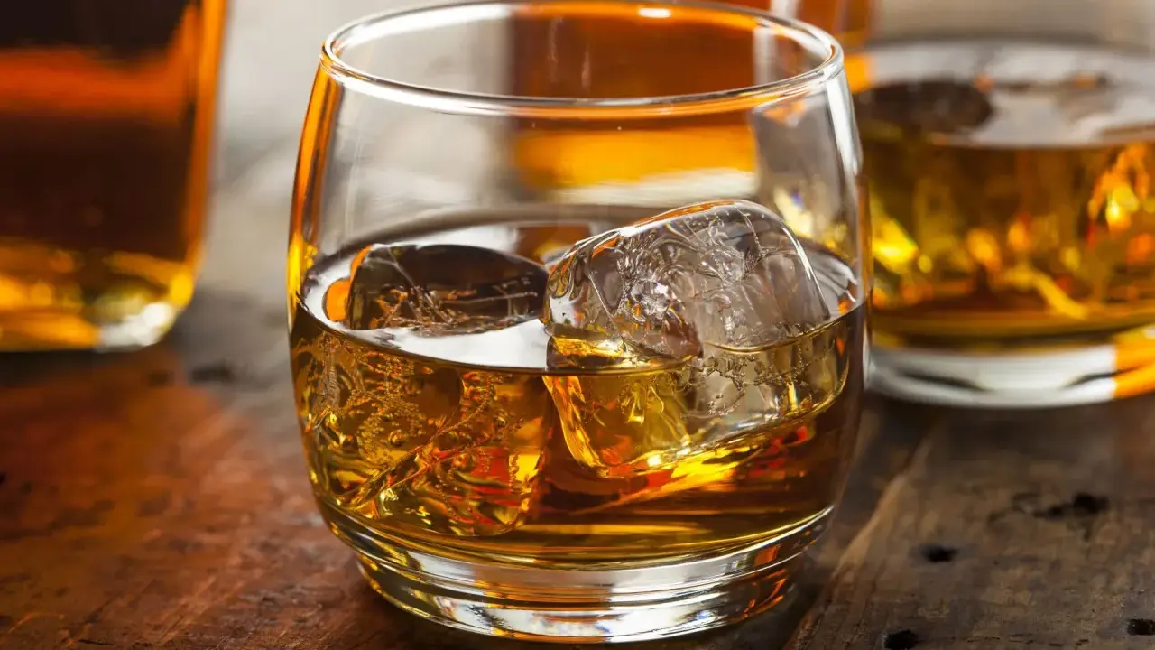 Szklanka złocistego trunku z lodem, otoczona butelkami. Czy to whisky szkocka czy irlandzka? Trudno zgadnąć, ale wygląda pysznie.
