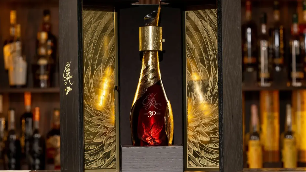 Elegancka, złota butelka z 30 letnią whisky Eagle Rare w ozdobnym, drewnianym pudełku z motywem piór.