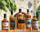 Pięć butelek szkockiej whisky: Edradour, Antiquary, Nomad, Claymore i Whyte & Mackay, stojących na drewnianym stole.