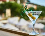 Idealny martini aperitivo z dwiema oliwkami, ozdobiony zielonymi wstążkami, na tle letniego krajobrazu.
