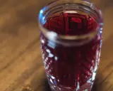 Kryształowy kieliszek wypełniony rubinową nalewką z winogron, stojący na drewnianym blacie.