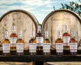 Butelki whisky BenRiach stoją przed beczkami, które zdradzają, skąd pochodzi whisky.