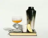Szklanka z drinkiem, shaker, cytryna i książka. Idealne akcesoria, by dowiedzieć się, z czym pić amarula.