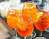 Cztery orzeźwiające Aperol Spritz z lodem i plasterkami pomarańczy, gotowe do świętowania lata.