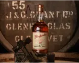 Butelka Glenfarclas 10 Year Old, jedna z 10 najlepszych whisky, na tle beczki. Młotek sugeruje rzemiosło.