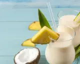 Dwa orzeźwiające koktajle pina colada z mlekiem, ozdobione kawałkami ananasa i liśćmi, na tle połówek kokosa.