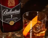 Orzeźwiający drink: whisky z wodą gazowaną, lodem i skórką pomarańczy, obok butelka Ballantine's.