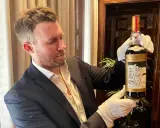 Mężczyzna w białych rękawiczkach prezentuje butelkę The Macallan 60 Year Old, jedną z najdroższych whisky świata.