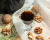 Nalewka z zielonych orzechów na spirytusie w kieliszku, otoczona łuskami i połówkami orzechów włoskich.