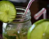 Orzeźwiający mohito drink, z widocznymi składnikami: limonką i miętą, w szklanym słoiku z rurką.