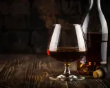 Kieliszek brandy obok butelki i korka na drewnianym stole.