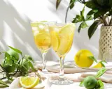 Dwa orzeźwiające drinki z lodem i plasterkami cytryny, idealne na upalne dni. Obok leżą świeże cytryny i zielone owoce.