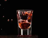 Wściekły pies drink, moneta spada do kieliszka z czerwonym płynem, tworząc fontannę.