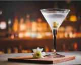 Martini extra dry z oliwkami, idealny do wieczornego relaksu. Na blacie stoi kieliszek z drinkiem i biały kwiatek.