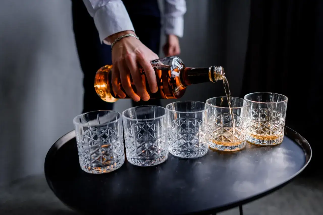 Elegancki mężczyzna nalewa whisky do kieliszków. Idealny dzień whisky, by uczcić wyjątkowe chwile.