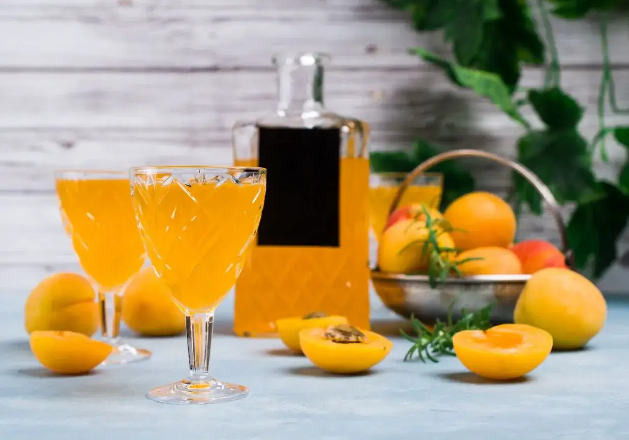 Idealny likier brzoskwiniowy przepis: świeże brzoskwinie, aromatyczny likier w kieliszkach i butelce, wszystko gotowe do degustacji.