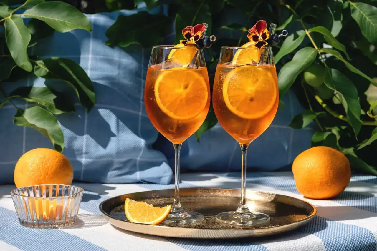 Dwa Aperol Spritz z pomarańczą i kwiatkiem, idealne na lato. Prosty aperol przepis na orzeźwiający drink.