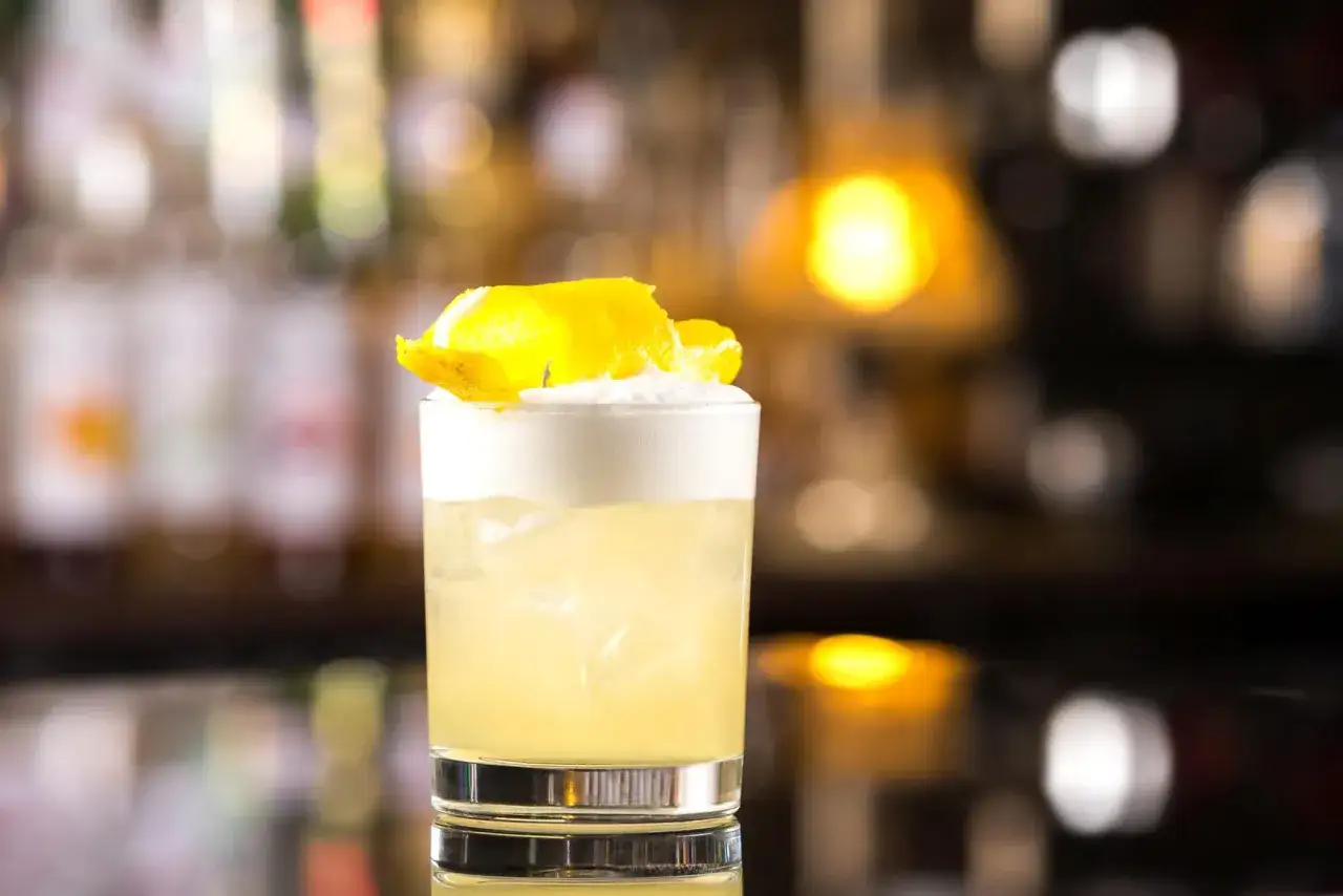 Orzeźwiający whisky sour z pianką i skórką cytrynową, idealny na wieczór w barze.