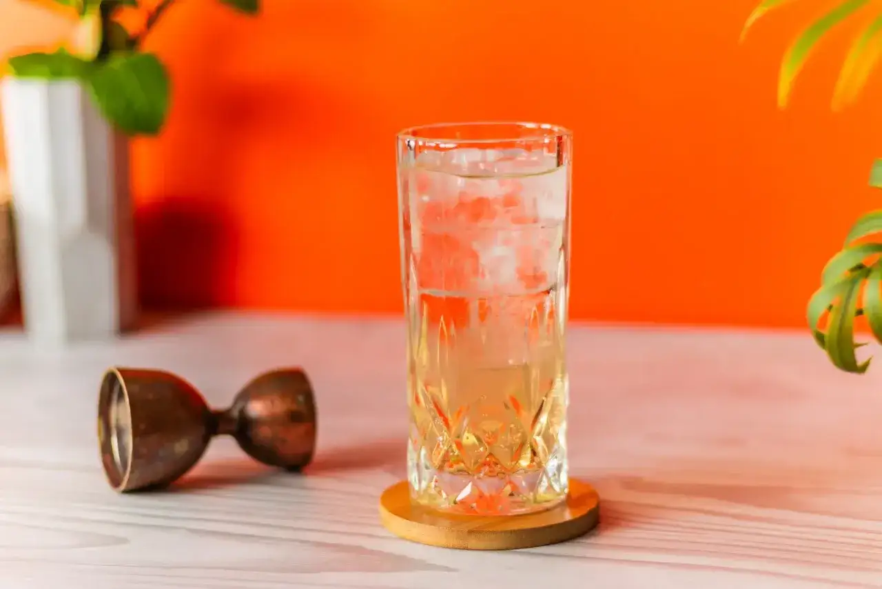 Orzeźwiający drink: whisky z wodą gazowaną, kostkami lodu i miedzianką barmańską na stole.