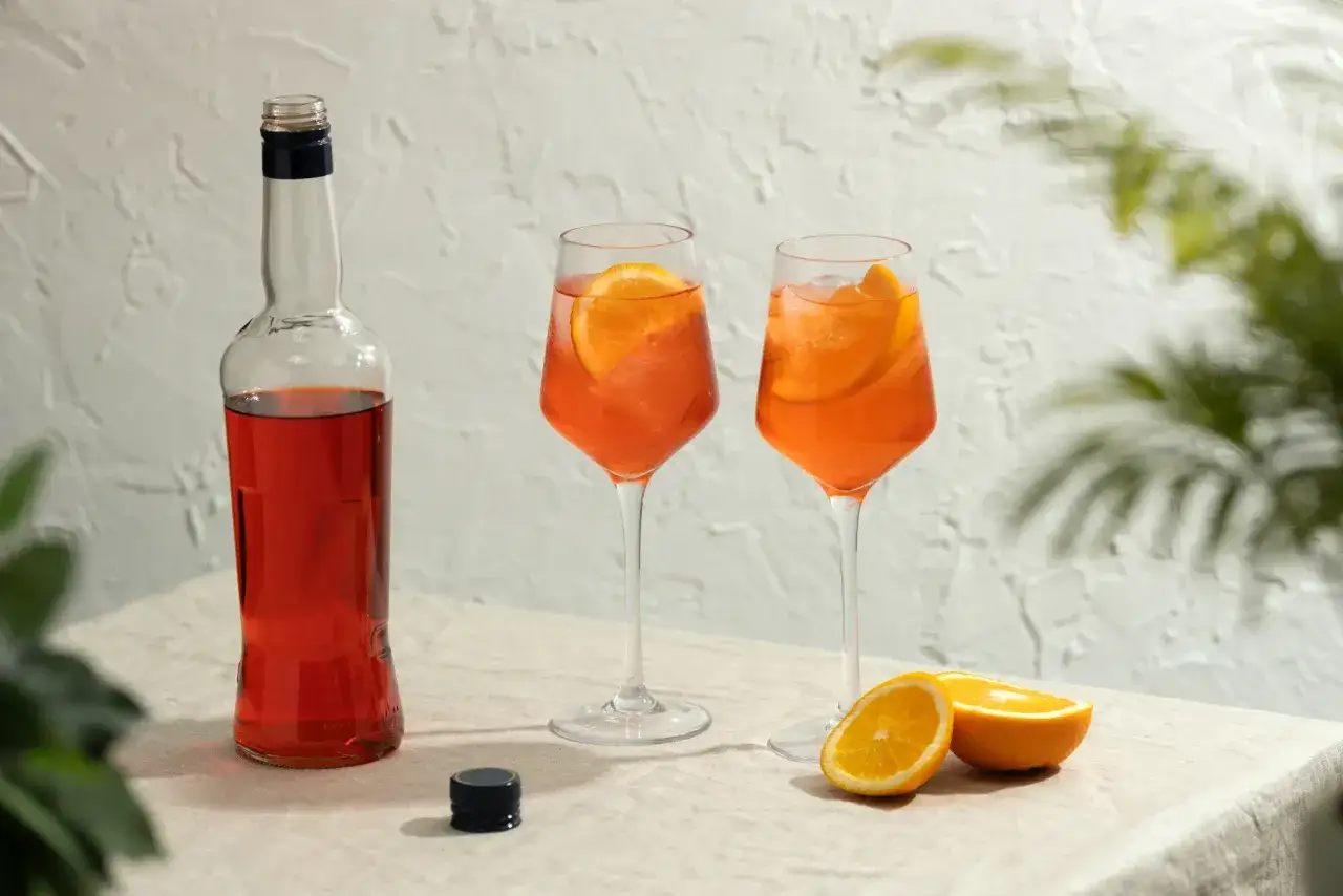 Dwa drinki Aperol Spritz z pomarańczą i butelka Aperolu. Idealne na letnie popołudnie, a jakie prosecco do Aperola? Wybierz wytrawne!
