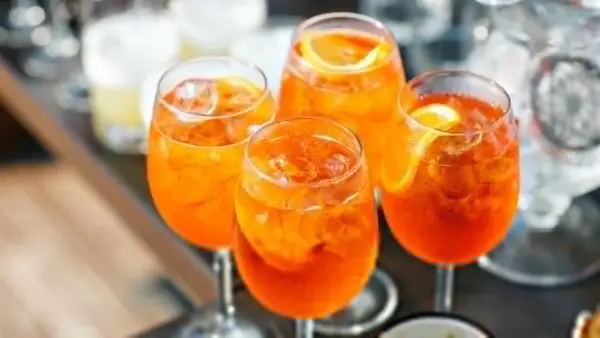 Cztery orzeźwiające Aperol Spritz z lodem i plasterkami pomarańczy, gotowe do świętowania lata.