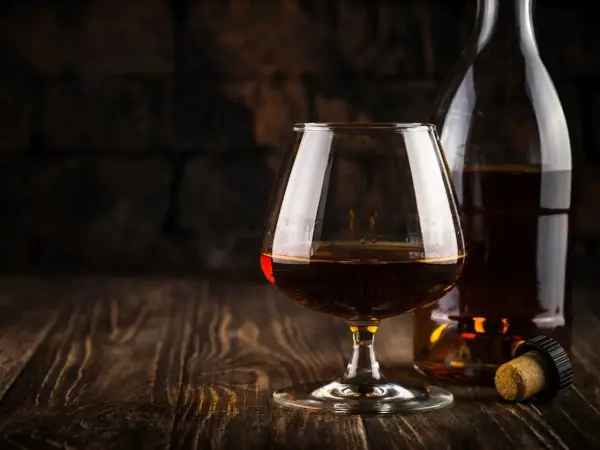 Kieliszek brandy obok butelki i korka na drewnianym stole.