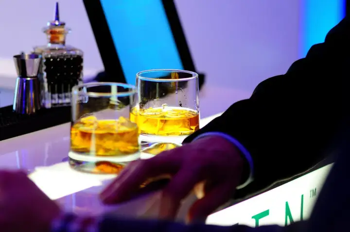 Dwa kieliszki złocistej whisky na barze, idealne na dzień whisky. Dłoń w garniturze sięga po drinka.