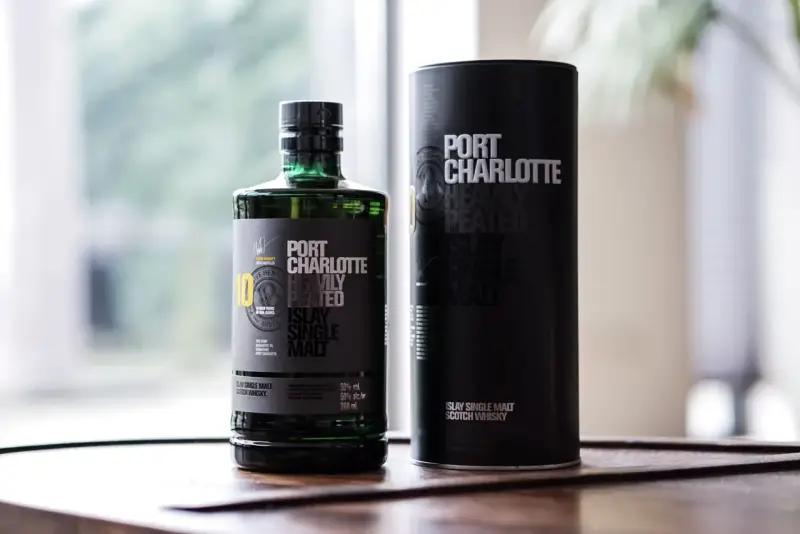 Port Charlotte Heavily Peated 10, whisky single malt z Islay, w zielonej butelce i czarnej tubie.